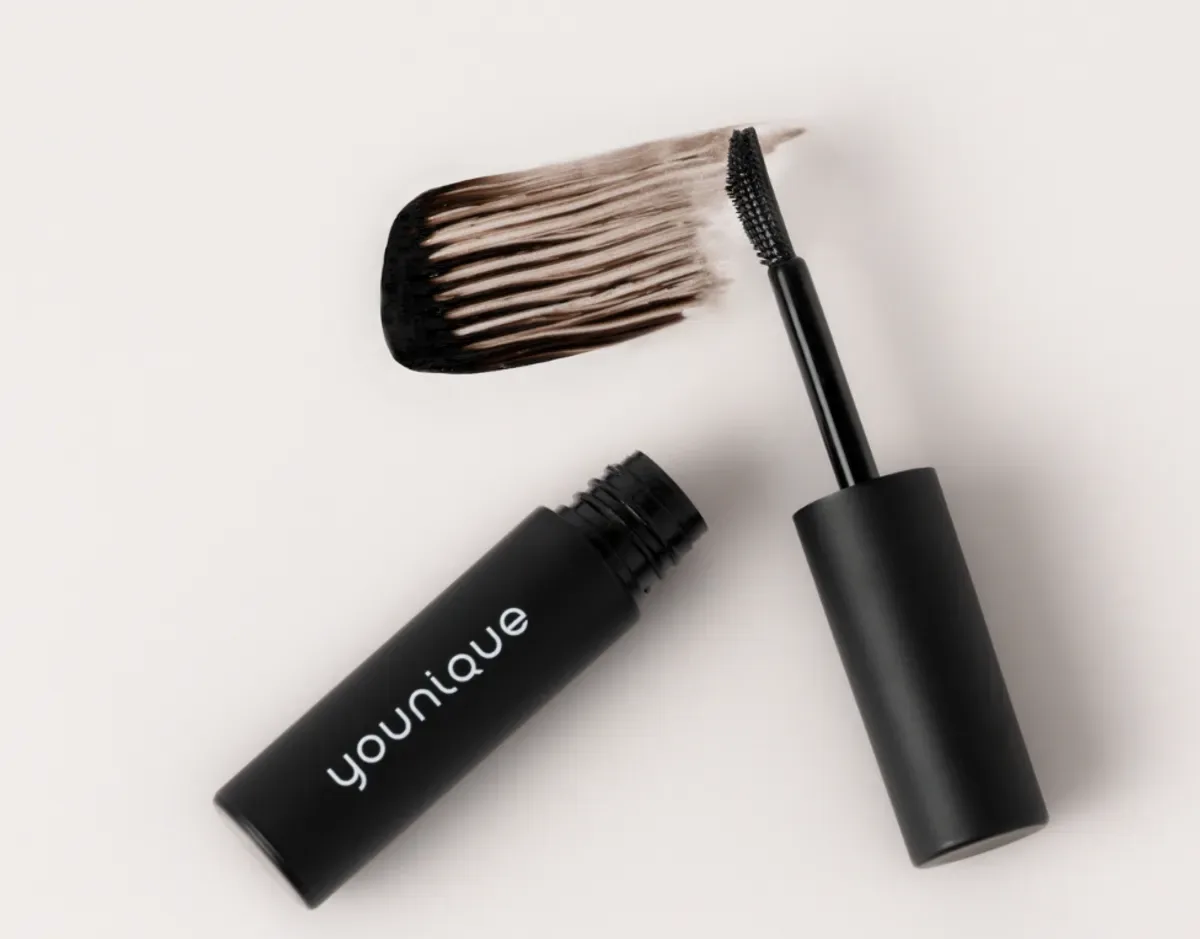 YOUNIQUE BARE·YOU eyebrow gel – tips : open tube and brush cap lying flat with a taupe-brown stroke of gel