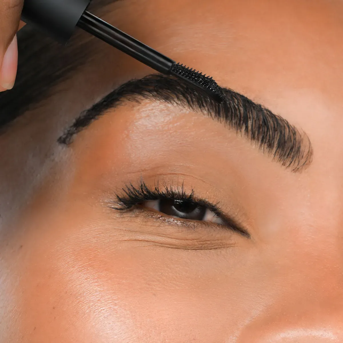 YOUNIQUE BARE·YOU eyebrow gel : close-up of a thick brown brow brushed upwards on tanned skin