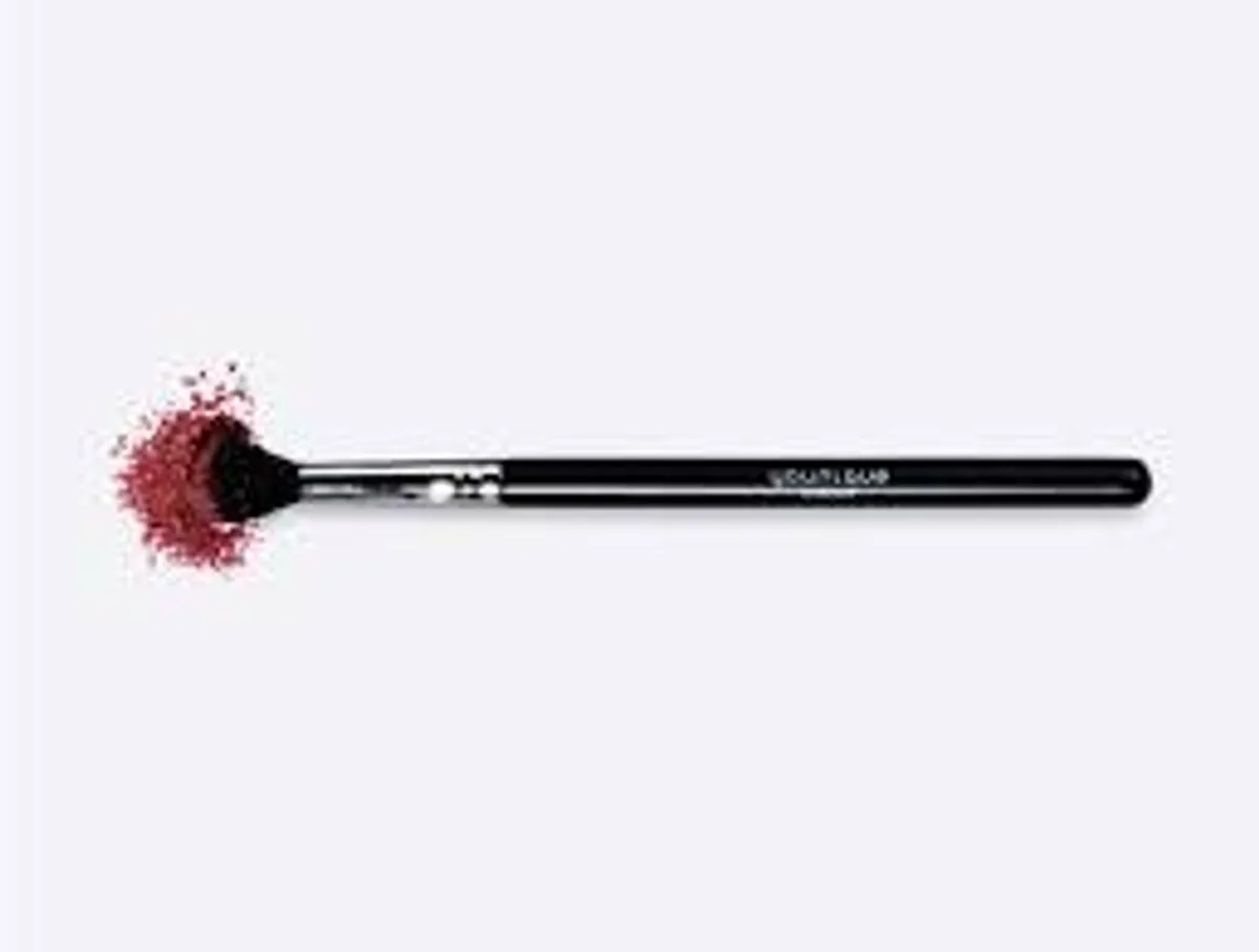 Pincel de esfumar YOUNIQUE – conselho: pincel com cerdas pretas colocado ao lado de uma sombra de olhos em pó cor de framboesa