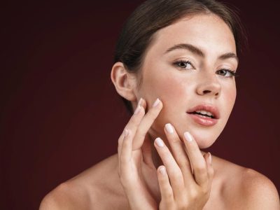 Image of alluring shirtless woman looking at camera and touching her clean fresh face isolated over red background